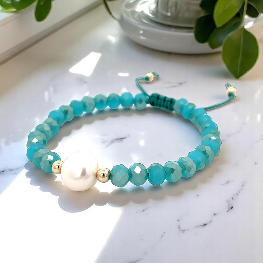 Turquoise beaded bracelet with a pearl and gold accents on a marble surface.