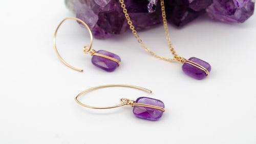 Gold jewelry set with purple gemstones on a white background