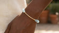 Aquamarine stone bar bracelet on hand, featuring glossy blue gemstone beads and gold-filled curved bar accent.


