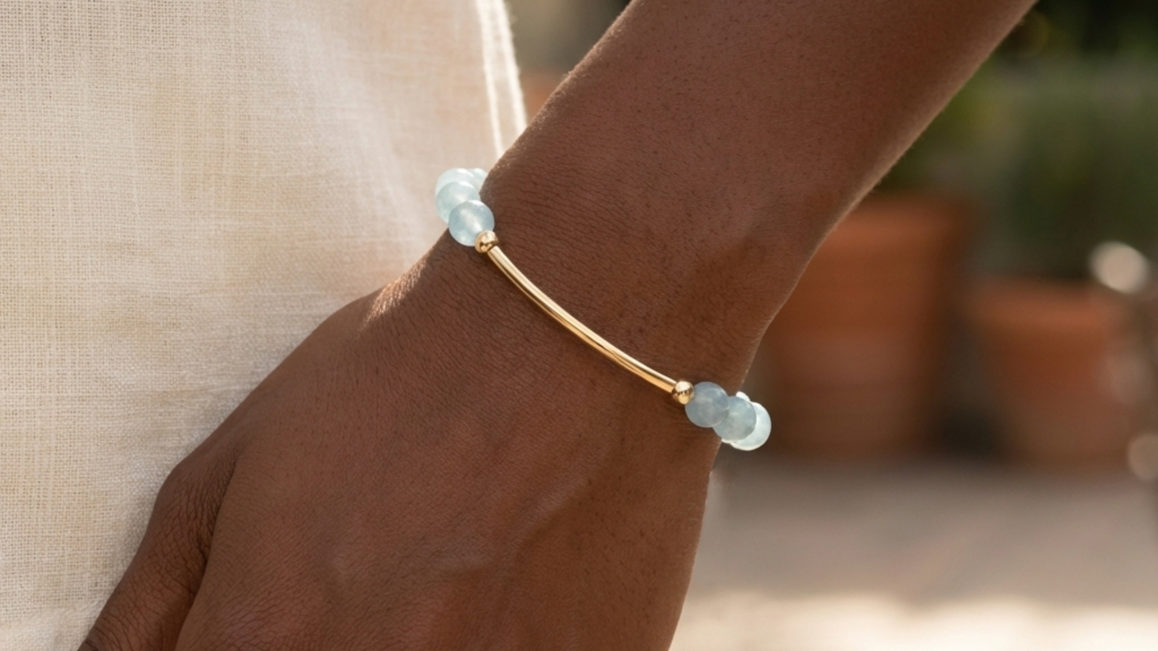 Aquamarine stone bar bracelet on hand, featuring glossy blue gemstone beads and gold-filled curved bar accent.



