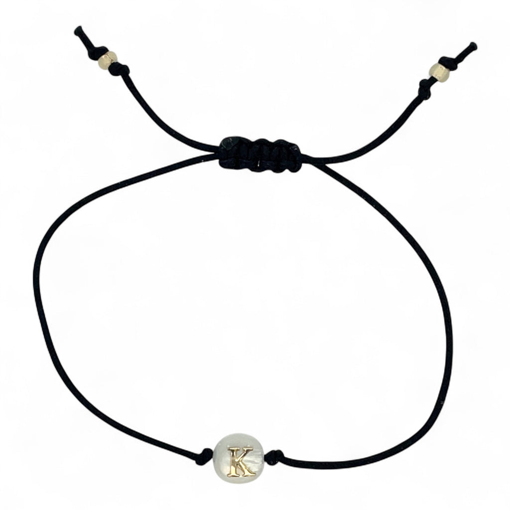 Black cord bracelet with a gold and silver charm on a white background