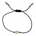 Black cord bracelet with a gold and silver charm on a white background