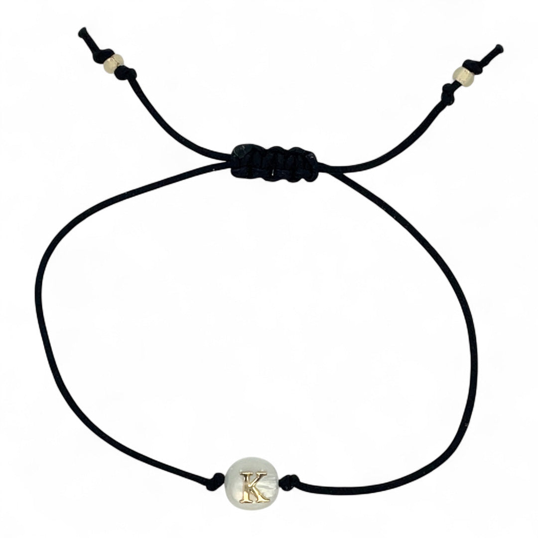 Black cord bracelet with a gold and silver charm on a white background