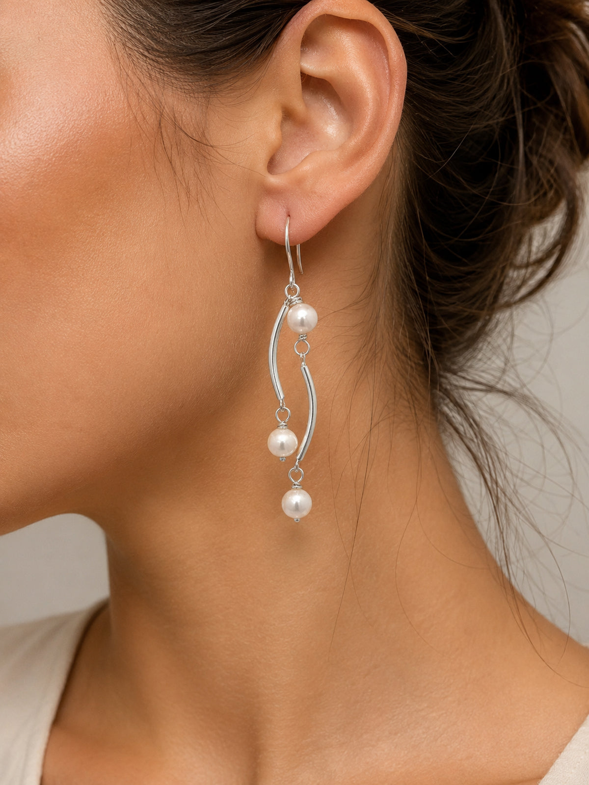 Close-up of a woman wearing silver earrings with pearls on a neutral background