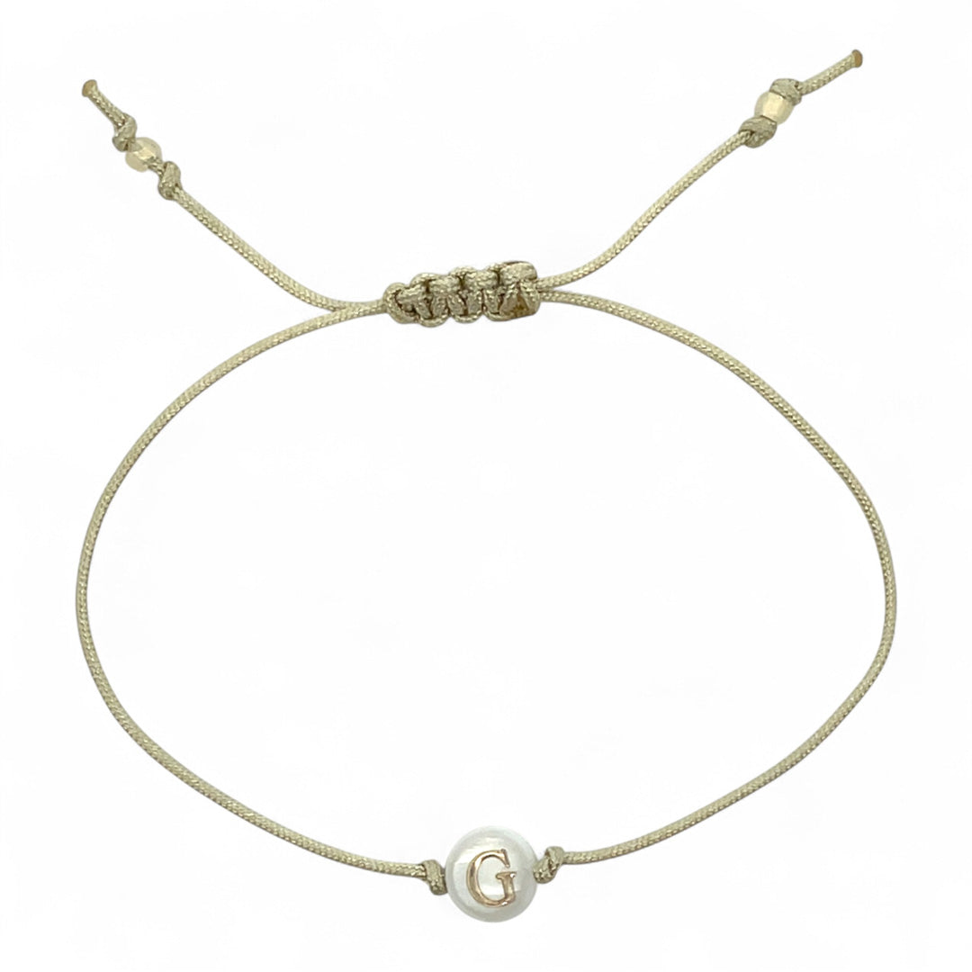 Beige bracelet with a small round bead featuring the letter 'G' on a white background