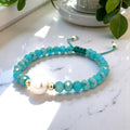 Turquoise beaded bracelet with a pearl and gold accents on a marble surface.