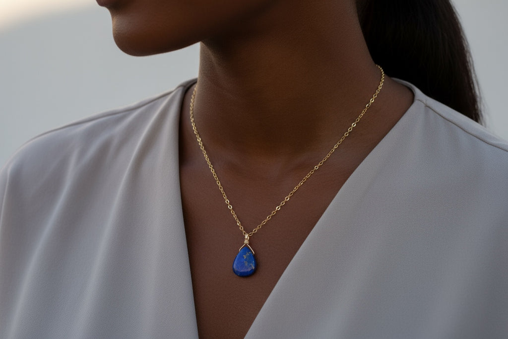Woman wearing a gold necklace with a blue lapis lazuli  pendant against a neutral background
