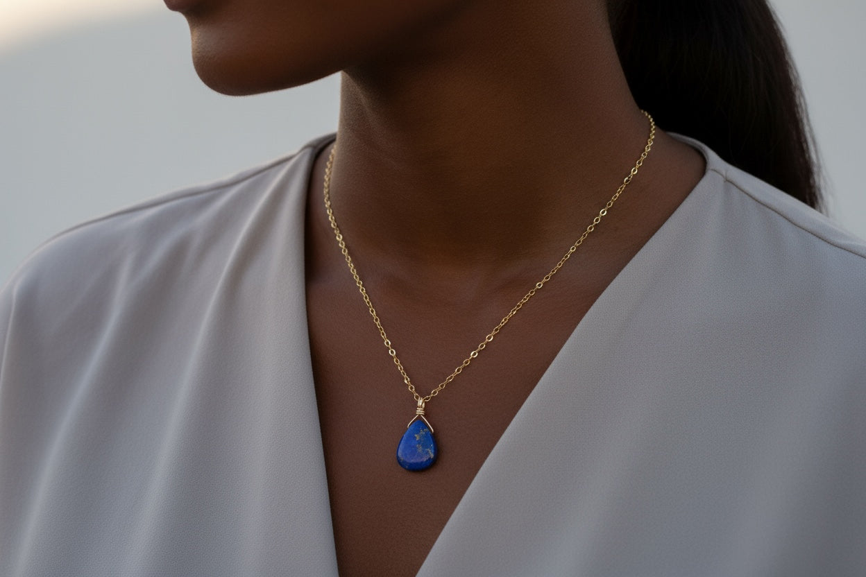 Woman wearing a gold necklace with a blue lapis lazuli  pendant against a neutral background
