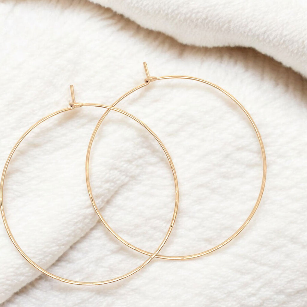 Close-up of large hand-forged gold hoop earrings in yellow gold-filled, displayed on a fluffy blanket 