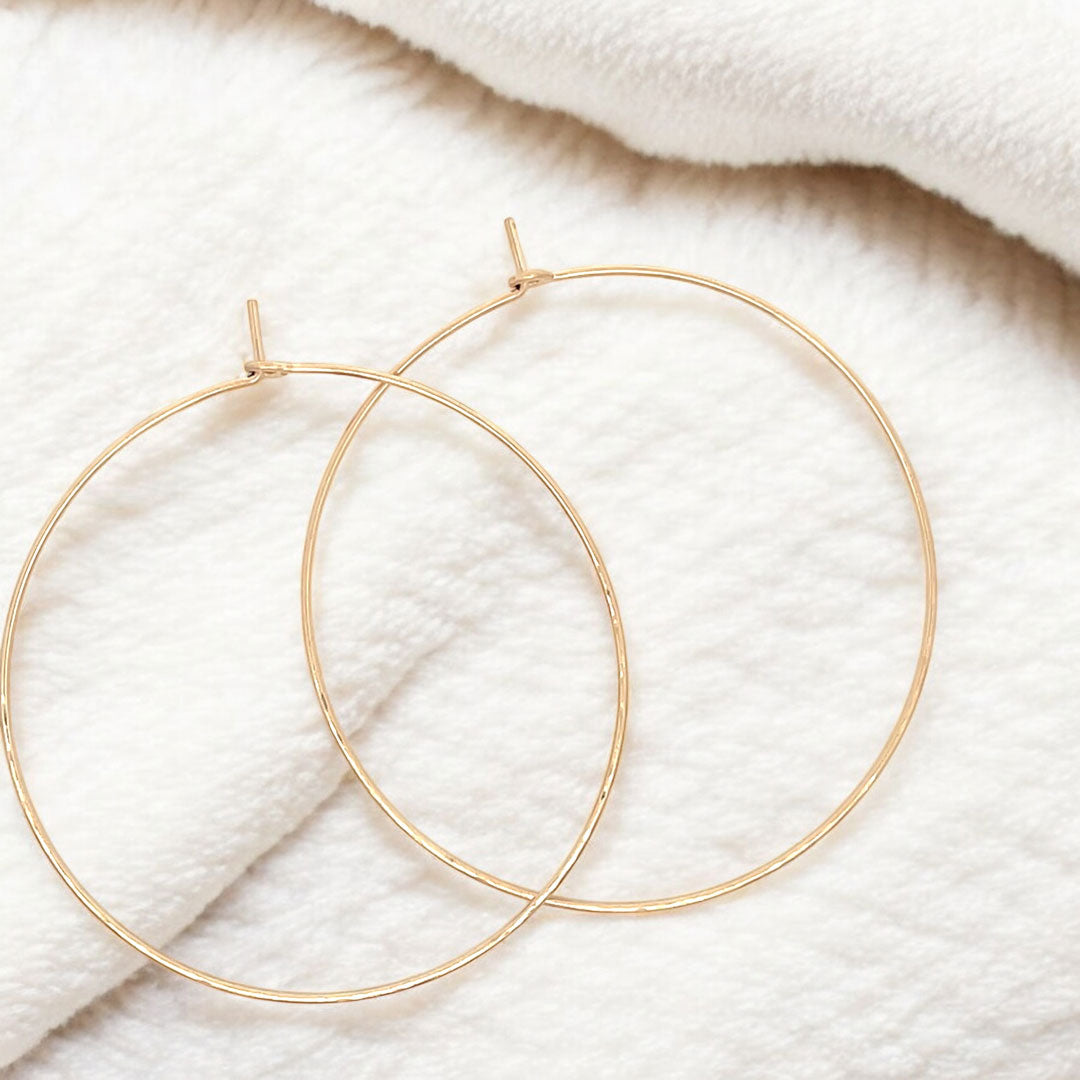 Close-up of large hand-forged gold hoop earrings in yellow gold-filled, displayed on a fluffy blanket 