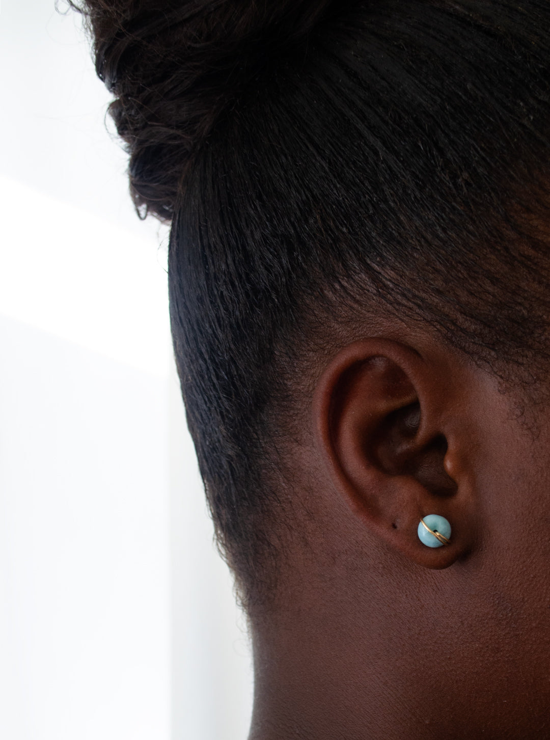 Close-up of an ear with a Larimar earring on a plain background