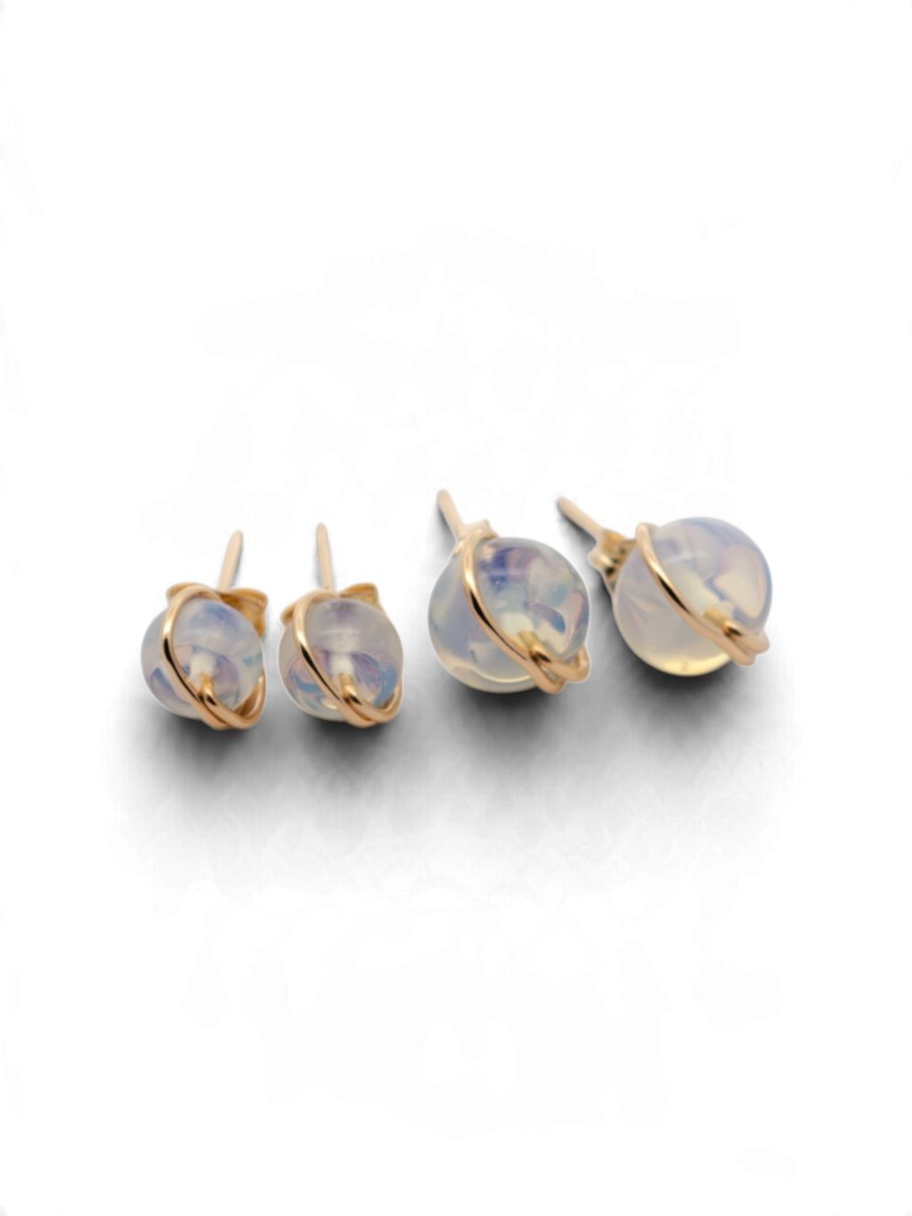 A set of gold-toned stud earrings with round iridescent opal-like cabochons, shown on a clean white background.