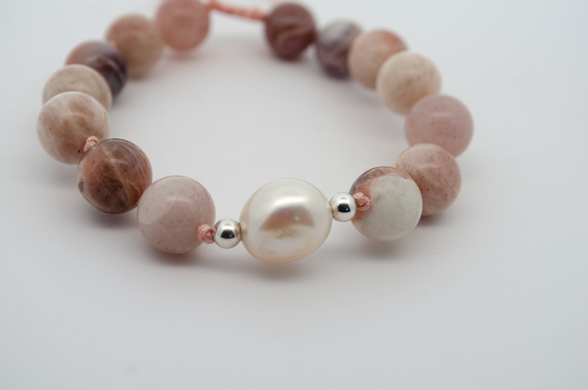 A beaded bracelet featuring a large white pearl bead at the center, flanked by round beads in soft pink, cream, and brown marbled stone, separated by small silver spacer beads on a white background.