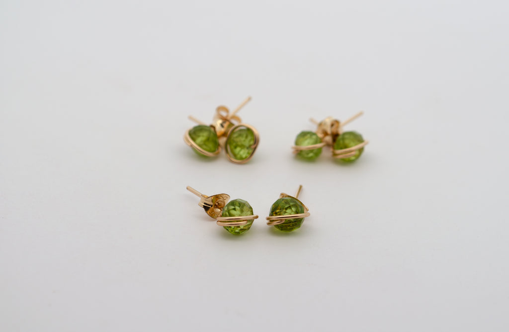 Three pairs of gold stud earrings with round green gemstones, shown on a plain light gray background.