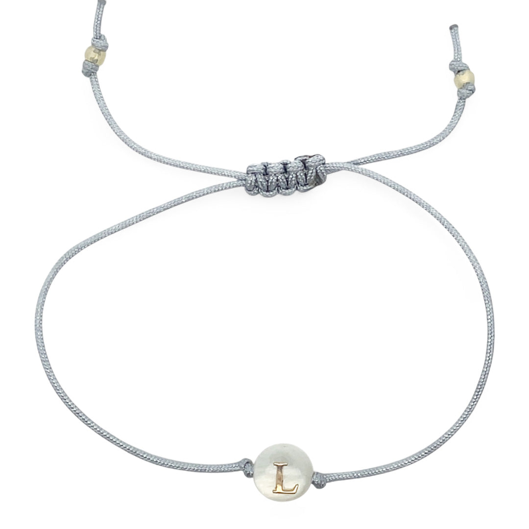 Bracelet with a white bead featuring a gold 'L' on a gray cord against a white background