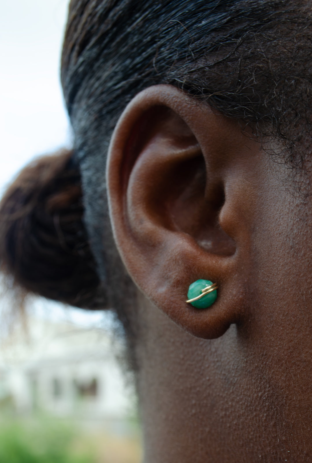 Close-up of an ear wearing a green earring with a blurred background