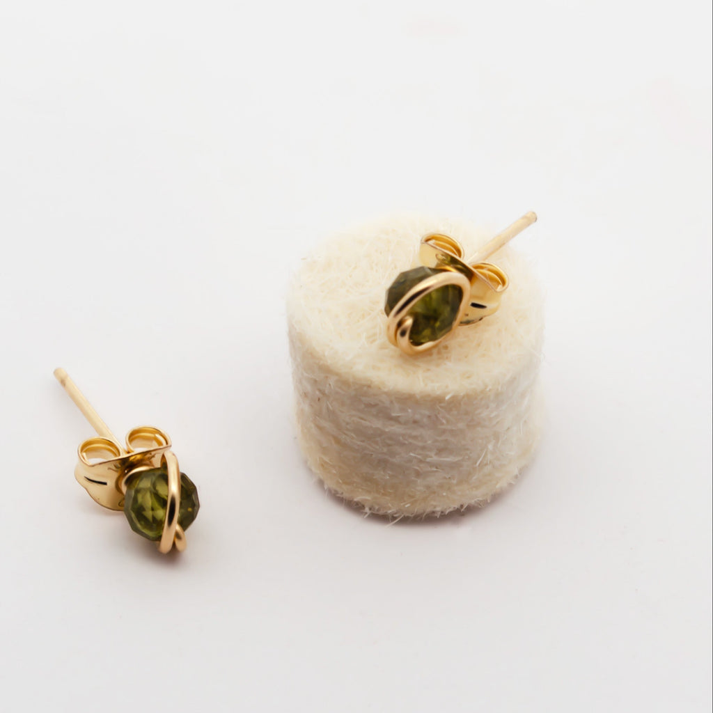 Gold earrings with green beads on a spool of thread against a white background