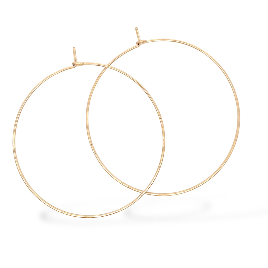 Close-up of large hand-forged gold hoop earrings in yellow gold-filled, displayed on a white backgroun