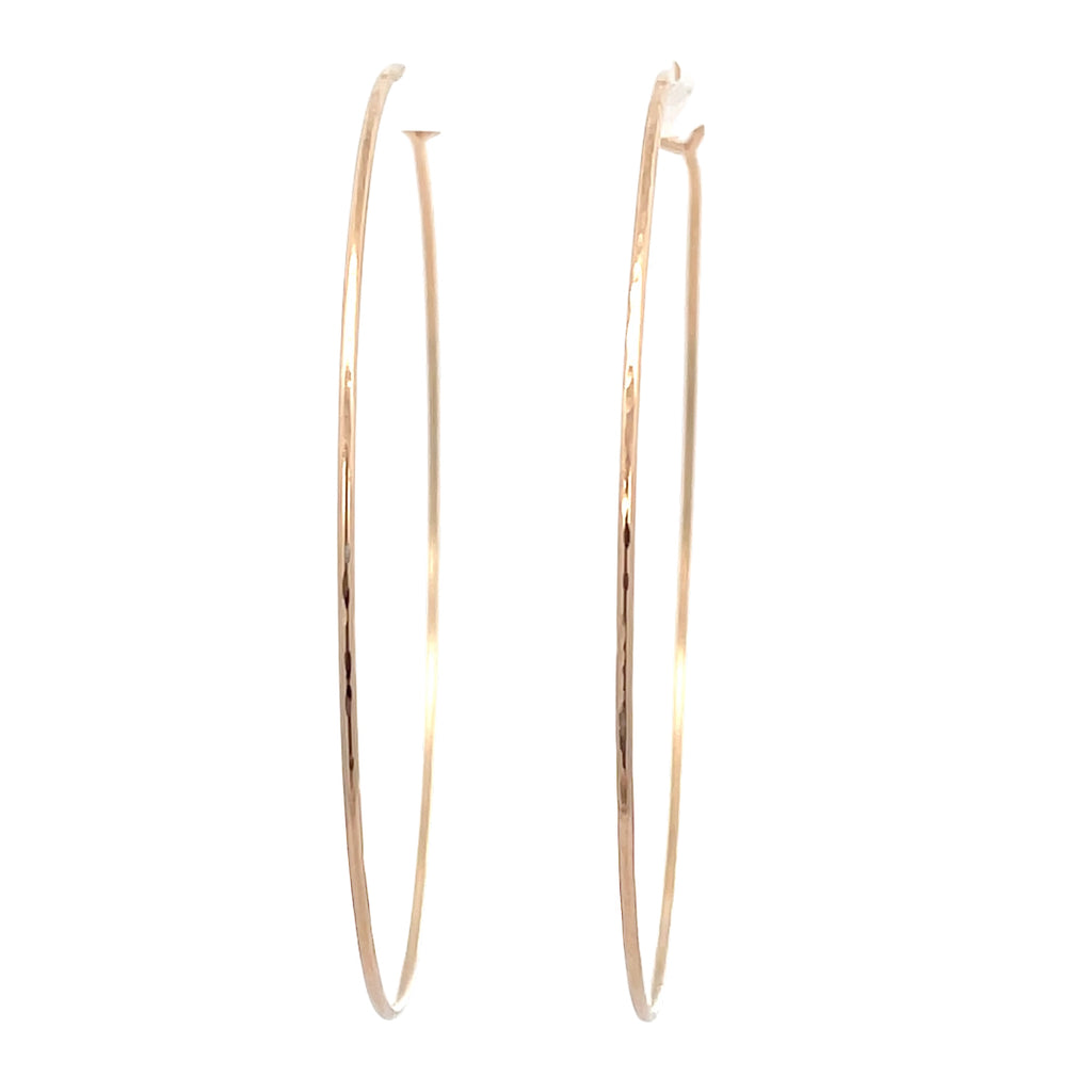 Close-up of large hand-forged gold hoop earrings in yellow gold-filled.