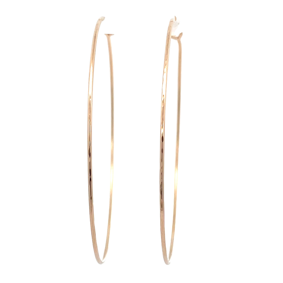 Close-up of large hand-forged gold hoop earrings in yellow gold-filled.