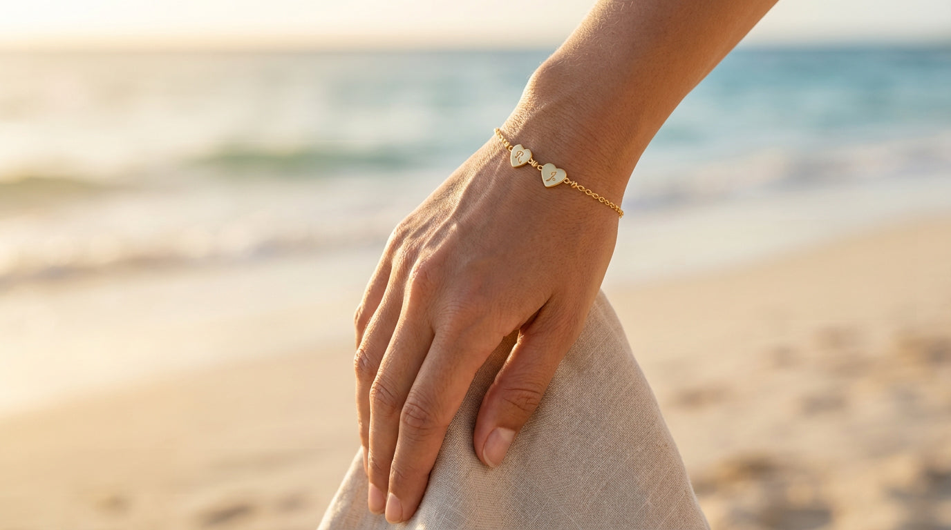 Hand wearing a gold bracelet with 2 heart linked on a beach