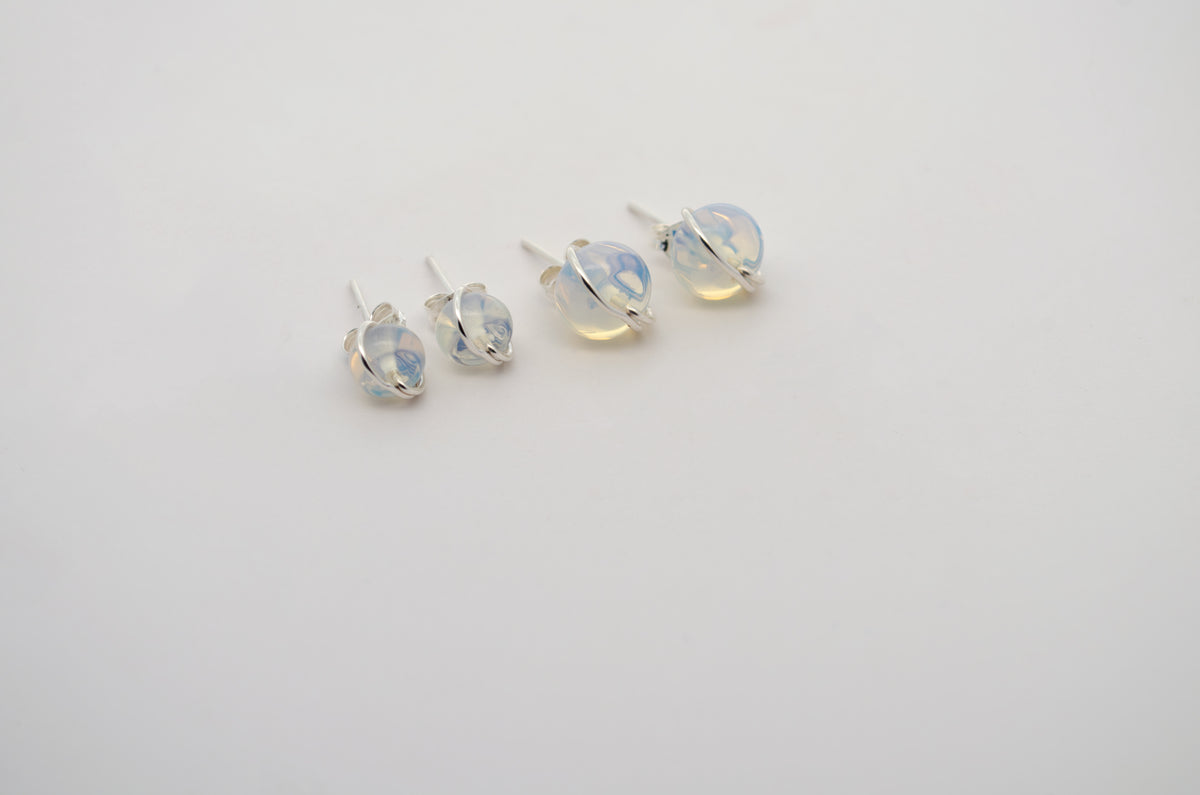 Four silver stud earrings with clear, iridescent glass beads that shimmer with blue and yellow hues, arranged on a plain white background.