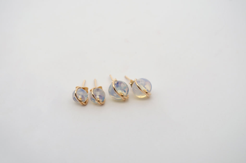 Three pairs of gold stud earrings with round, milky white gemstones, arranged on a plain white background.